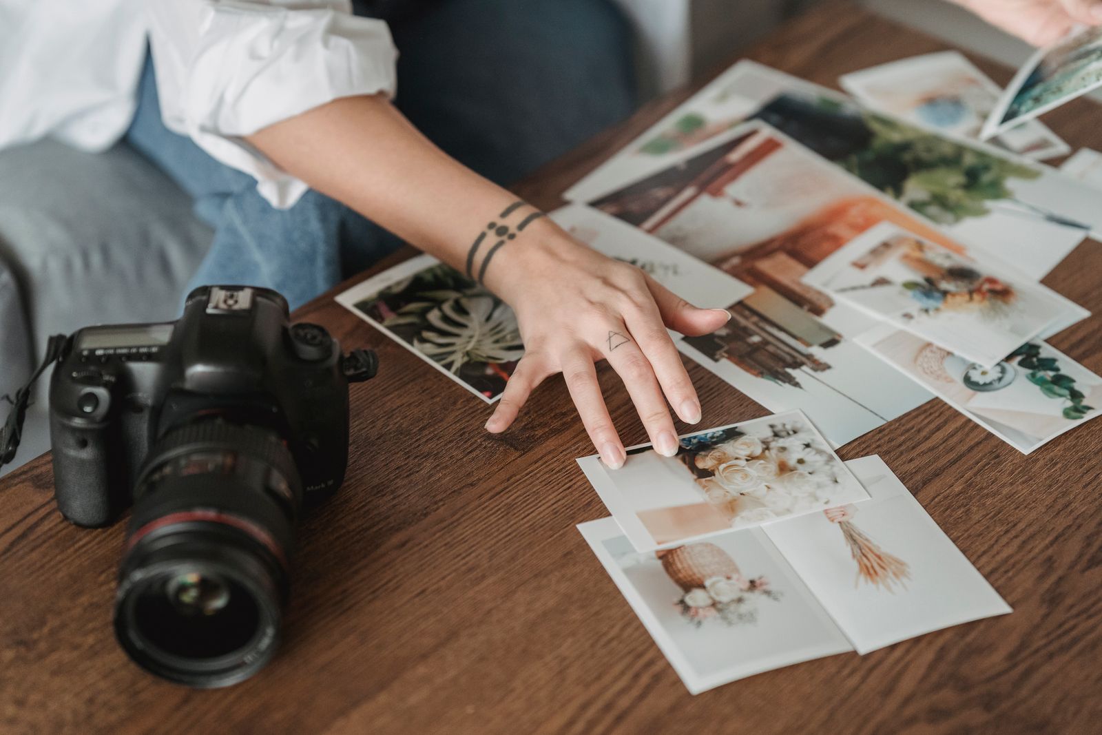 Photographer sorting printed photos on a wooden table beside a camera